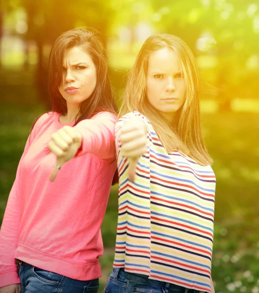 Two attractive girls show thumbs down against green nature backg — Stock Photo, Image