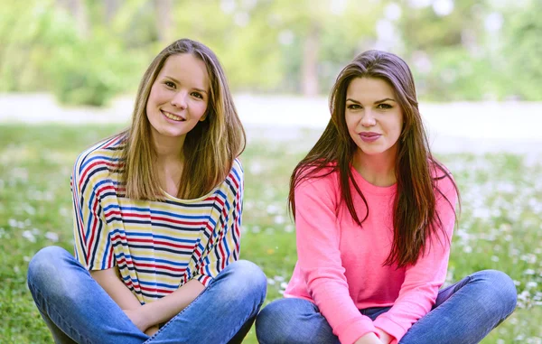 Två unga flicka vänner sitter på gräset vid sommardag — Stockfoto