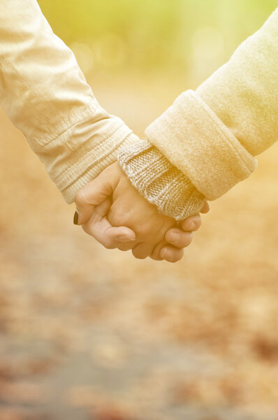 Closeup of couple holding hands while walking in park