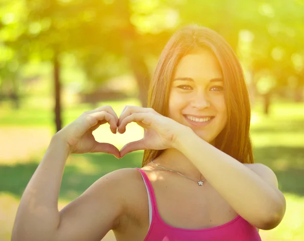 Menina adolescente bonito fazendo forma de coração com as mãos ao ar livre — Fotografia de Stock