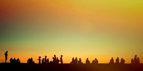 Grupp av unga människor som sitter på väggen vid solnedgången — Stockfoto