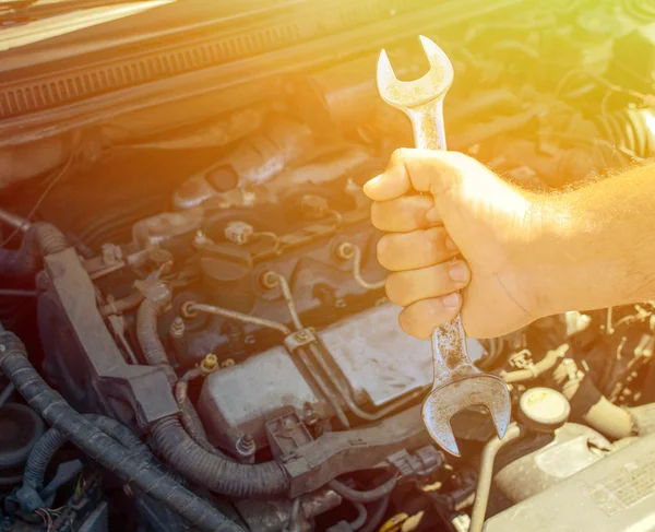 Ruka drží klíč proti auto motor — Stock fotografie