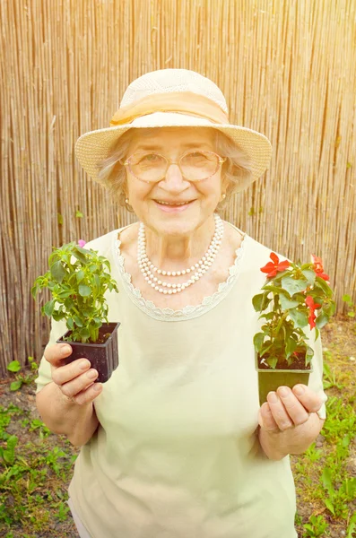 Gelukkig senior vrouw met bloemen in de tuin — Stockfoto