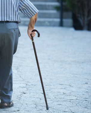 Yaşlı adam elleri tahta bir sopayla yürüyor.