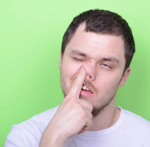 Portrait of a young man with his finger in his nose against gree — Stock Photo, Image