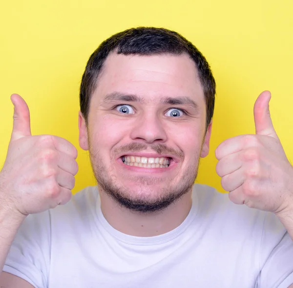 Portrait of with funny expression holding thumbs up against yell — Stock Photo, Image