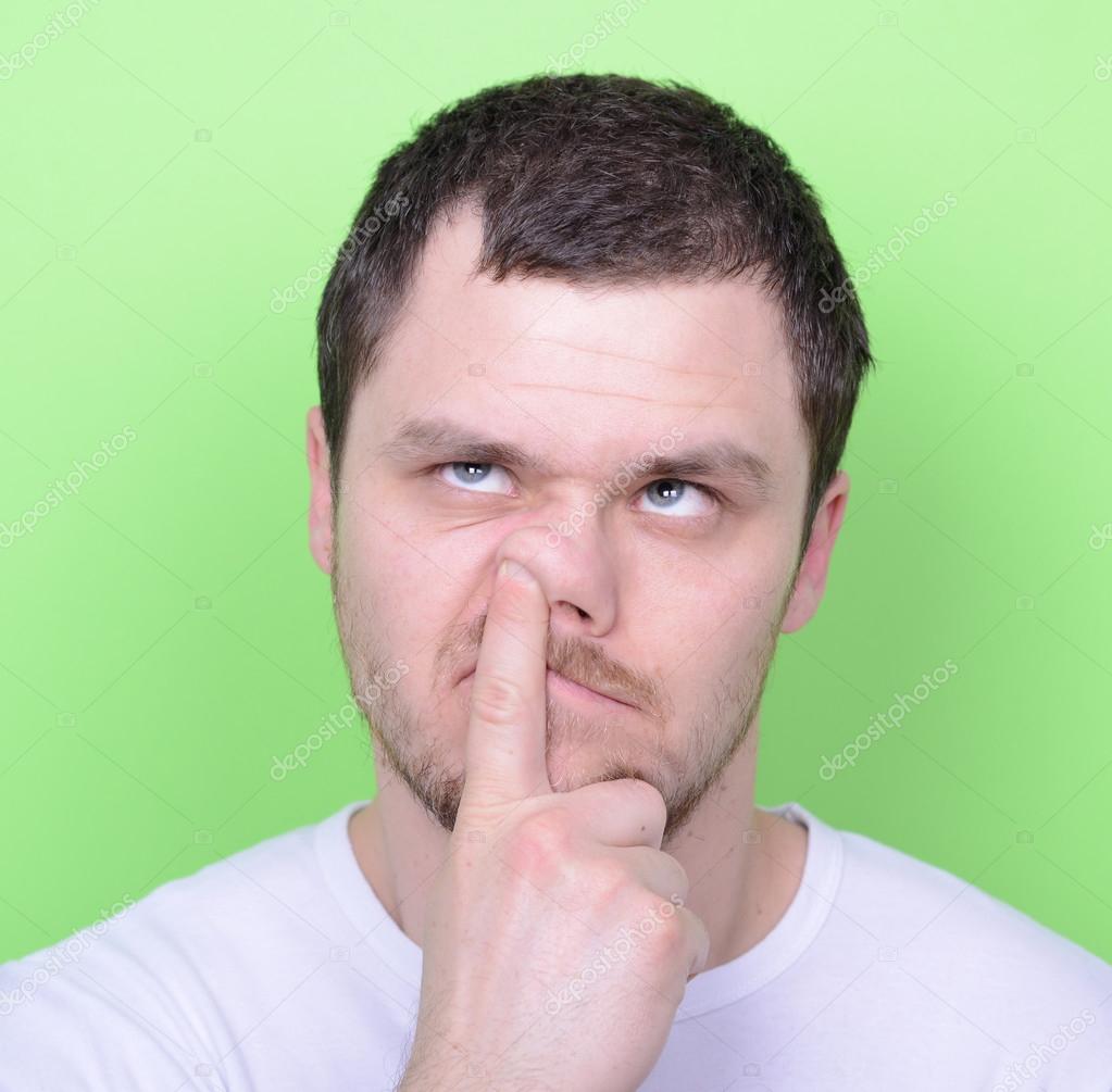Portrait of a young man with his finger in his nose against gree