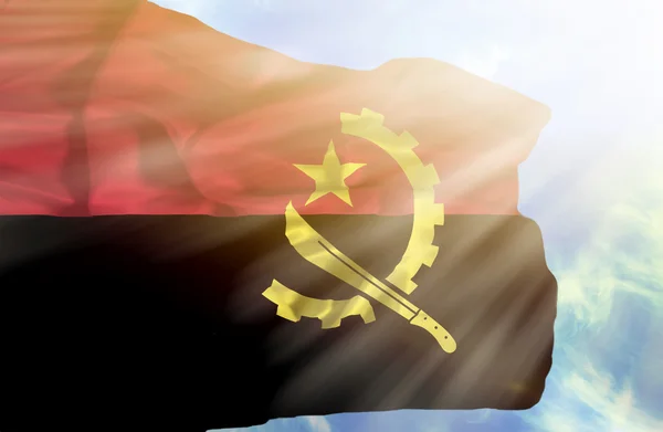 Angola schwenkt Flagge gegen blauen Himmel mit Sonnenstrahlen — Stockfoto