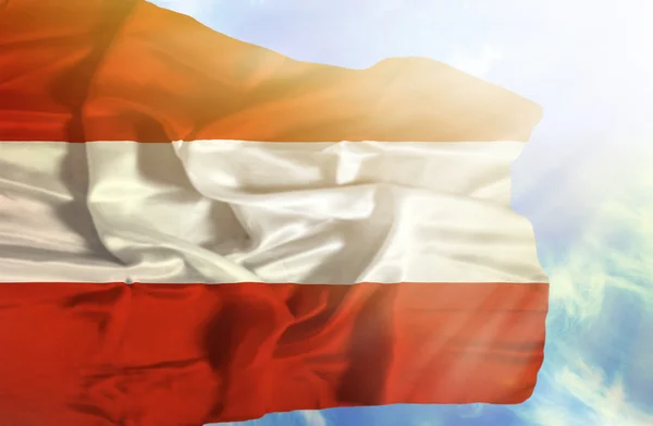 Österreich schwenkt Flagge gegen blauen Himmel mit Sonnenstrahlen — Stockfoto