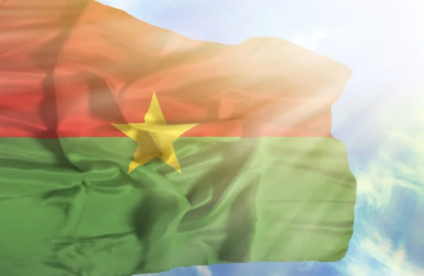 Drapeau du Burkina Faso agitant contre le ciel bleu avec des rayons de soleil — Photo