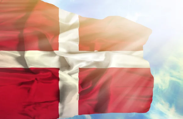 Дания машет флагом на фоне голубого неба с солнечными лучами — стоковое фото