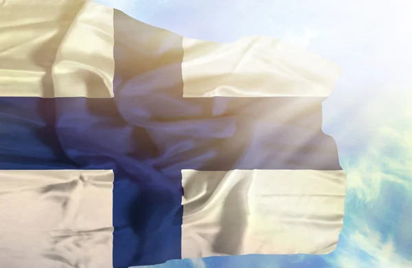 Finland viftande flagga mot blå himmel med solstrålar — Stockfoto