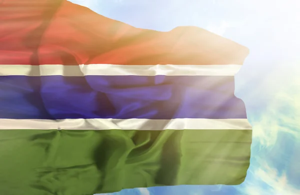 Gambia ondeando bandera contra el cielo azul con rayos de sol — Foto de Stock