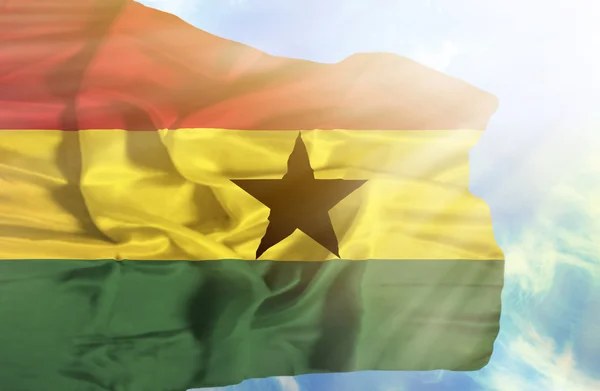 Ghana ondeando bandera contra el cielo azul con rayos de sol —  Fotos de Stock