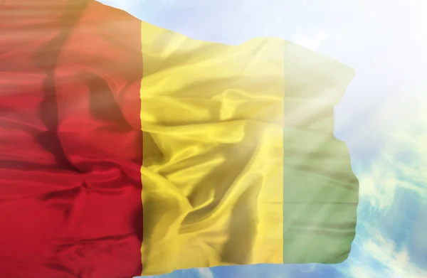 Guinée agitant le drapeau contre le ciel bleu avec des rayons de soleil — Photo