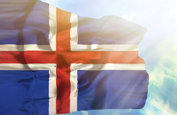Island schwenkt Flagge gegen blauen Himmel mit Sonnenstrahlen — Stockfoto
