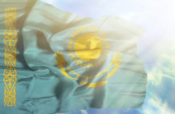 Kasachstan schwenkt Flagge gegen blauen Himmel mit Sonnenstrahlen — Stockfoto