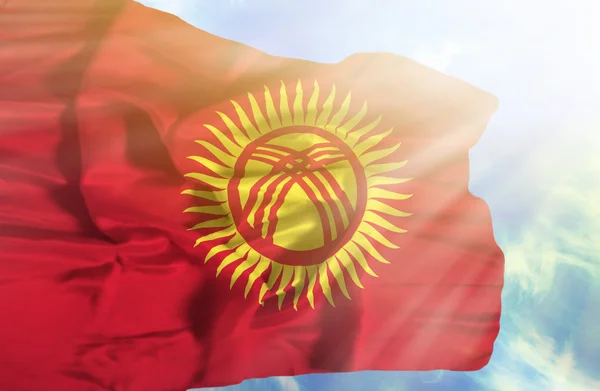 Kyrgyzstan waving flag against blue sky with sunrays — Stock Photo, Image