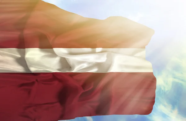 Latvia waving flag against blue sky with sunrays — Stock Photo, Image