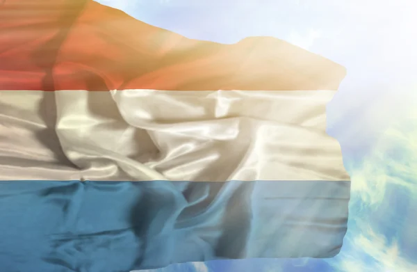Luxemburgo ondeando bandera contra el cielo azul con rayos de sol —  Fotos de Stock