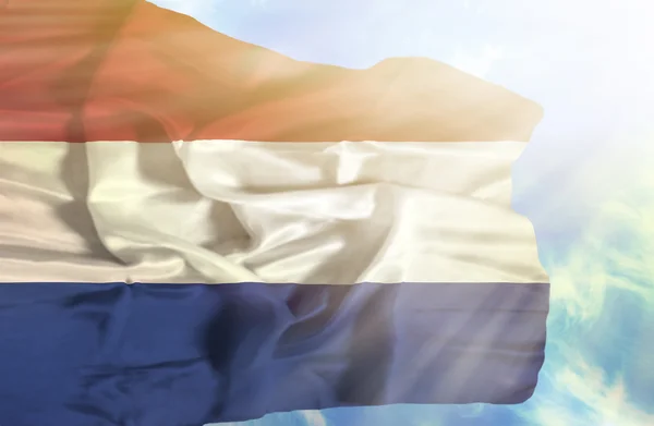 Nederländerna viftande flagga mot blå himmel med solstrålar — Stockfoto