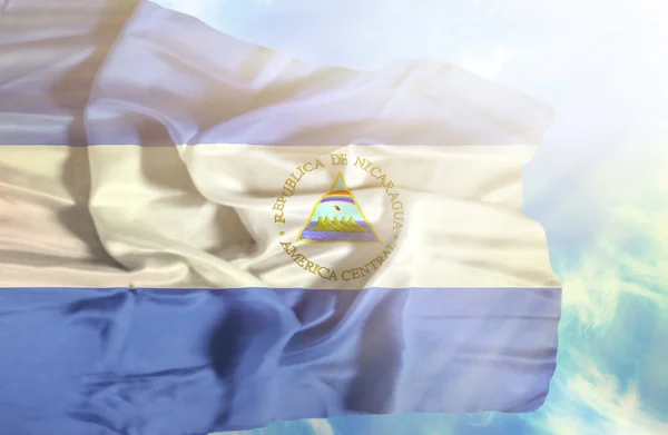 Nicaragua schwenkt Flagge gegen blauen Himmel mit Sonnenstrahlen — Stockfoto