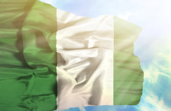 Nigeria schwenkt Flagge gegen blauen Himmel mit Sonnenstrahlen — Stockfoto