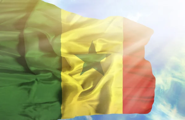 Senegal schwenkt Flagge gegen blauen Himmel mit Sonnenstrahlen — Stockfoto
