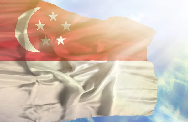 Singapura agitando bandeira contra o céu azul com raios de sol — Fotografia de Stock