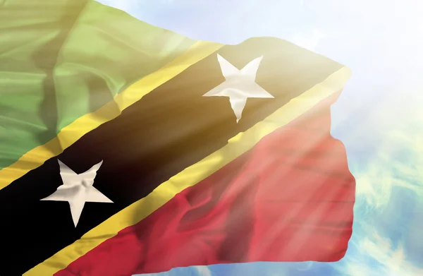 St kitts en nevis zwaaien vlag tegen blauwe hemel met zonnestralen — Stockfoto