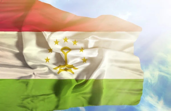 Tayikistán ondeando bandera contra el cielo azul con rayos de sol — Foto de Stock