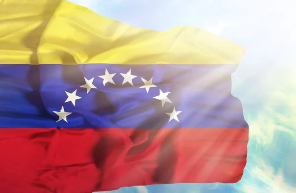 Venezuela schwenkt fahne gegen blauen himmel mit sonnenstrahlen — Stockfoto