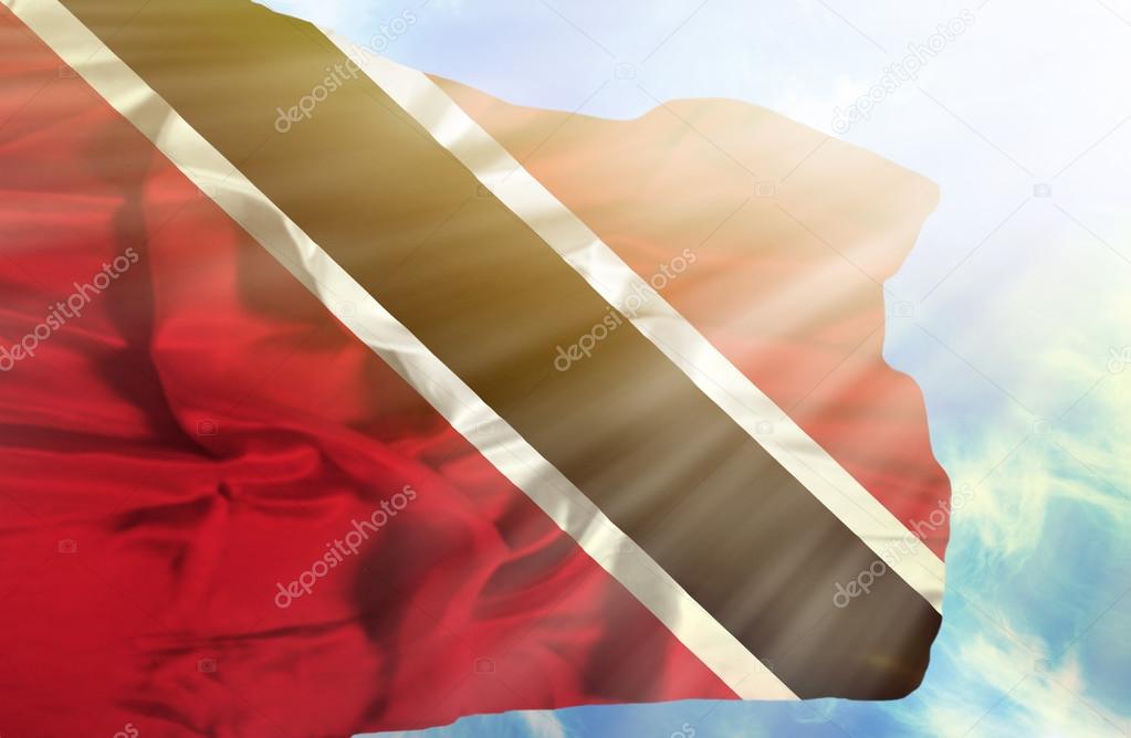 Trinidad and Tobago waving flag against blue sky with sunrays