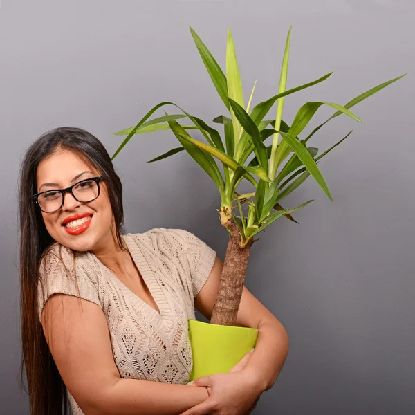 Hermosa mujer feliz sosteniendo planta en jarrón contra el backgro gris — Foto de Stock