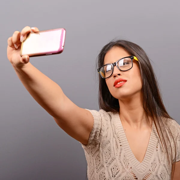 Портрет девушки, делающей селфи с сотовым телефоном против серого цвета — стоковое фото