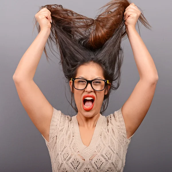 Portrait of a histerical woman pulling hair out against gray bac — Stock Photo, Image