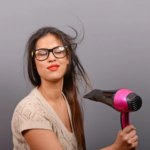 Retrato de una mujer sosteniendo secador de pelo sobre fondo gris — Foto de Stock