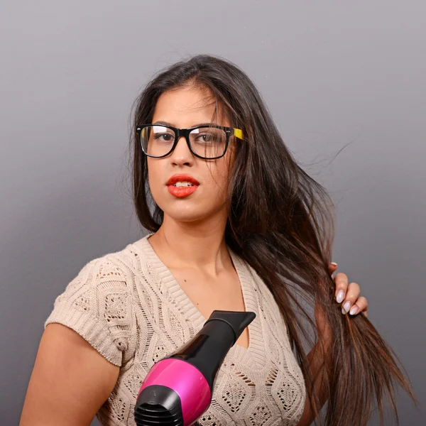 Portret kobiety, trzymając włosy suszarką na szarym tle — Zdjęcie stockowe
