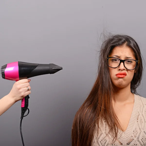 Retrato de una mujer sosteniendo secador de pelo sobre fondo gris —  Fotos de Stock