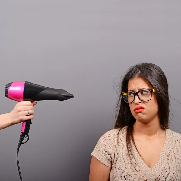 Retrato de una mujer sosteniendo secador de pelo sobre fondo gris — Foto de Stock