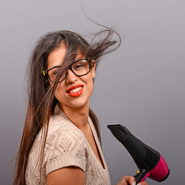 Portrait of a woman holding hair dryer against gray background
