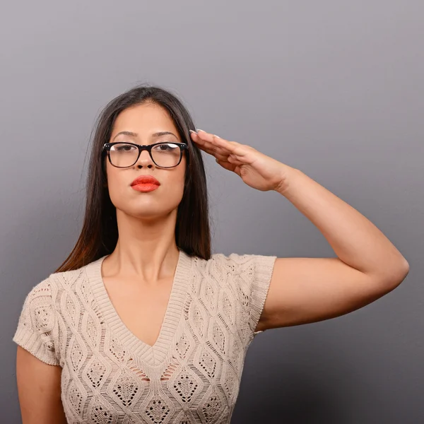 Portrait of serious woman saluting in casual clothes against gra — Stock Photo, Image