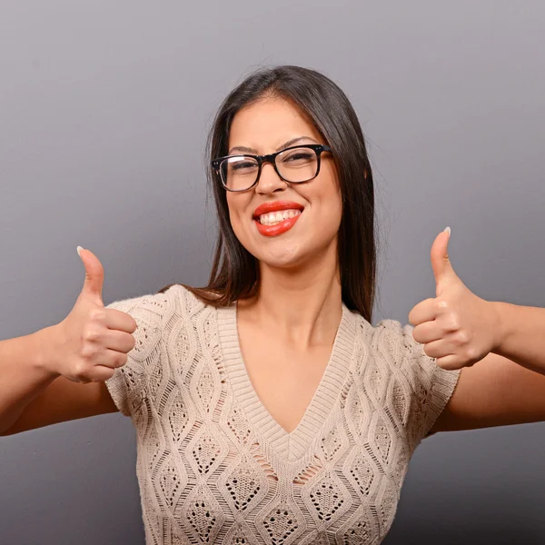 Portrait of happy woman holding thumbs up against gray backgroun — Stock Photo, Image