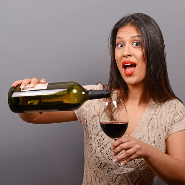 Portrait of woman holding wine bottle and glass against gray bac — ストック写真