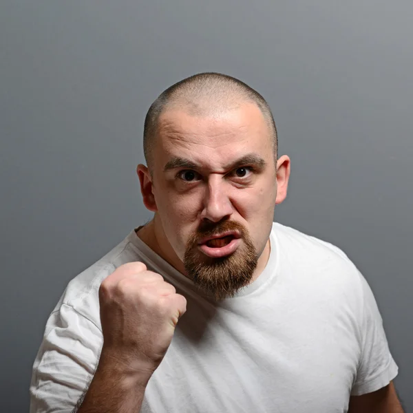 Portræt af en vred mand, der holder næver mod grå baggrund - Stock-foto