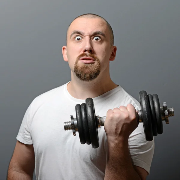 Retrato de un hombre divertido sosteniendo pesas contra fondo gris —  Fotos de Stock