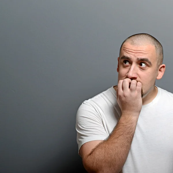 Portrait of a man biting nails and being scared against gray bac — Stock Photo, Image