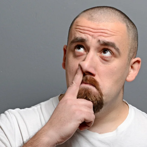 Portrait of a man putting finger in his nose against gray backgr — Stock Photo, Image