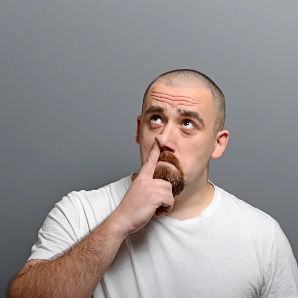 Portrait of a man putting finger in his nose against gray backgr — Stock Photo, Image