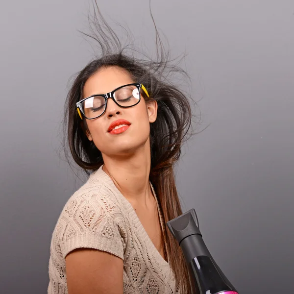 Portrait of a woman holding hair dryer against gray background Stock Photo